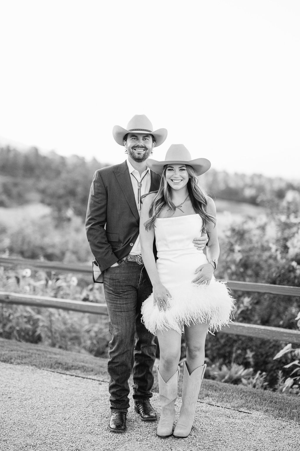 A couple poses together in black and white photos on a grassy hill, with one wearing cowboy boots and a white dress.