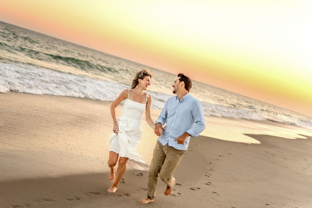 A couple runs playfully along the beach shoreline during a beautiful sunset.