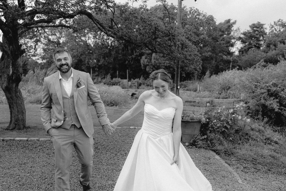 A black and white wedding photo sequence showing a couple sharing a playful moment outdoors in a garden setting.