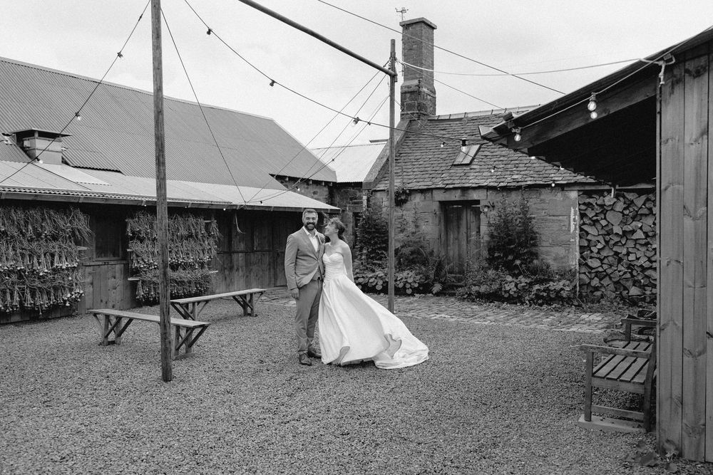 A rustic outdoor wedding venue with string lights and wooden structures shown in black and white photography.