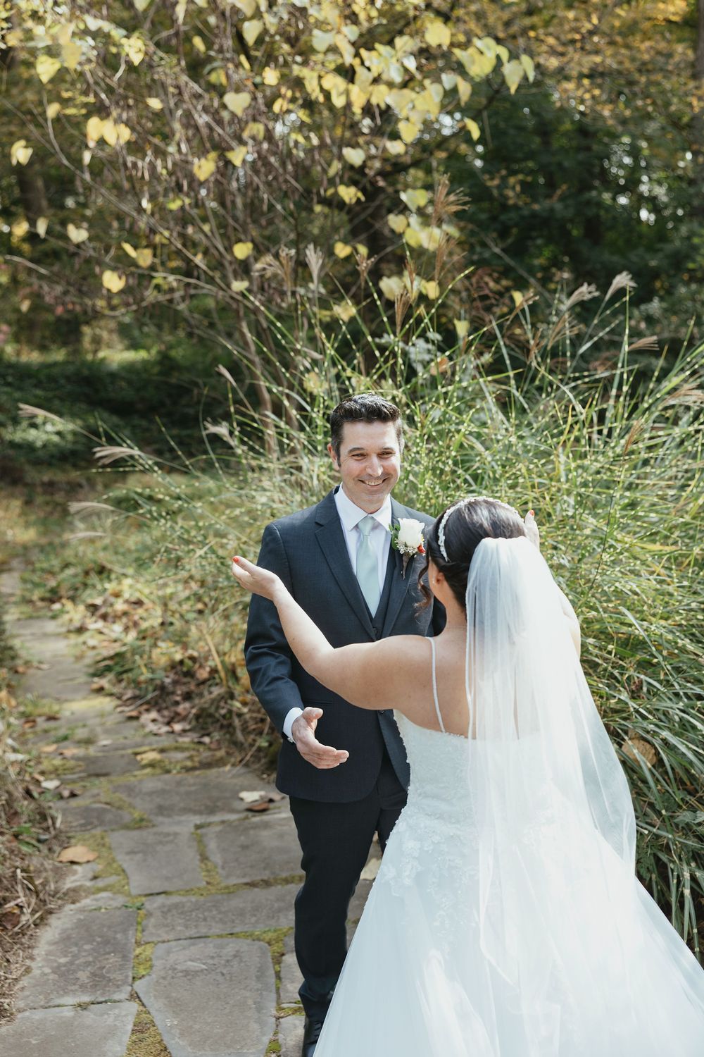 A joyful first look moment between newlyweds surrounded by lush greenery and autumn leaves.