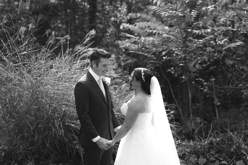 A couple in formal wedding attire shares an intimate moment together in a lush outdoor garden setting.
