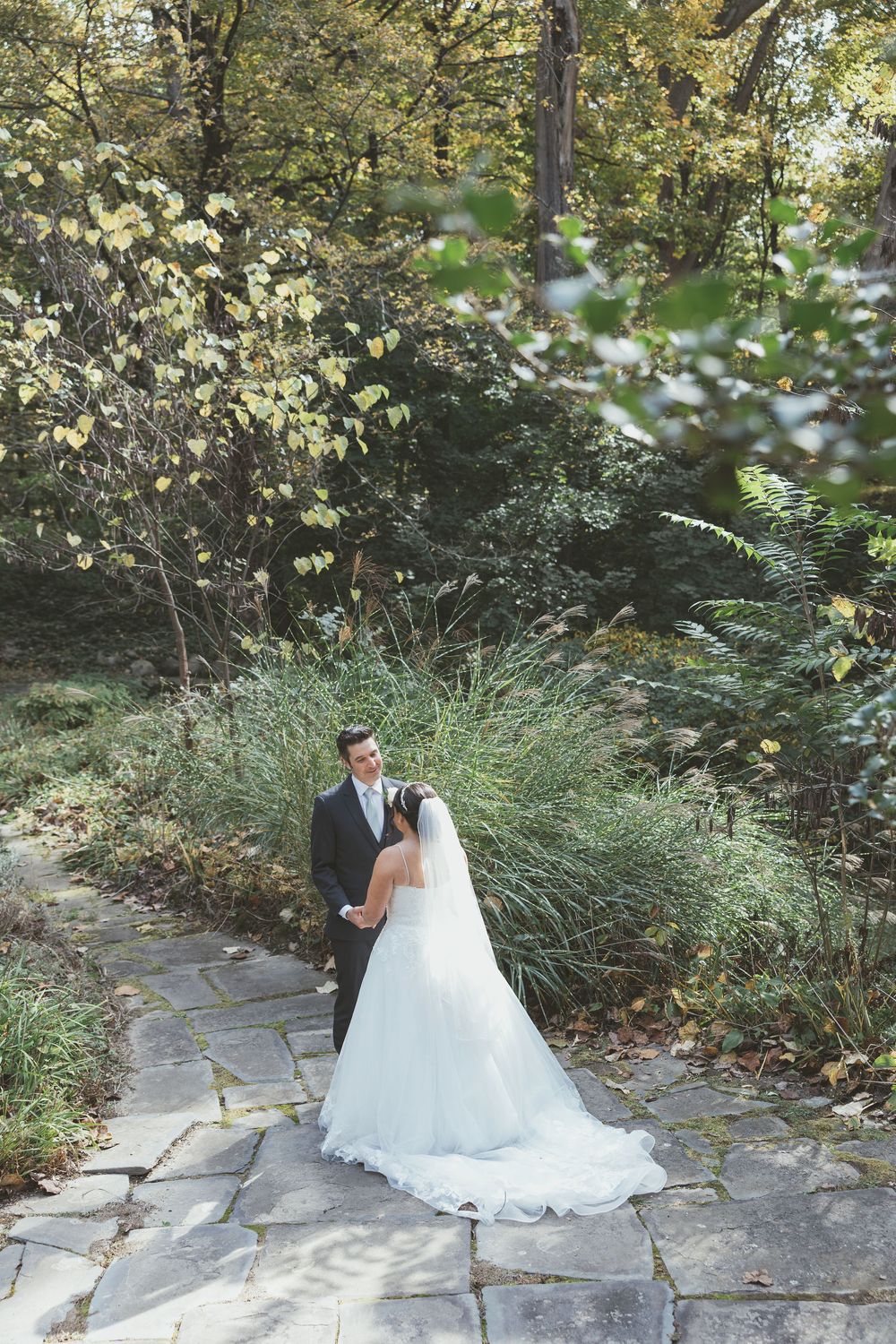 A couple shares a romantic moment on a stone path surrounded by lush greenery and trees in a garden setting.