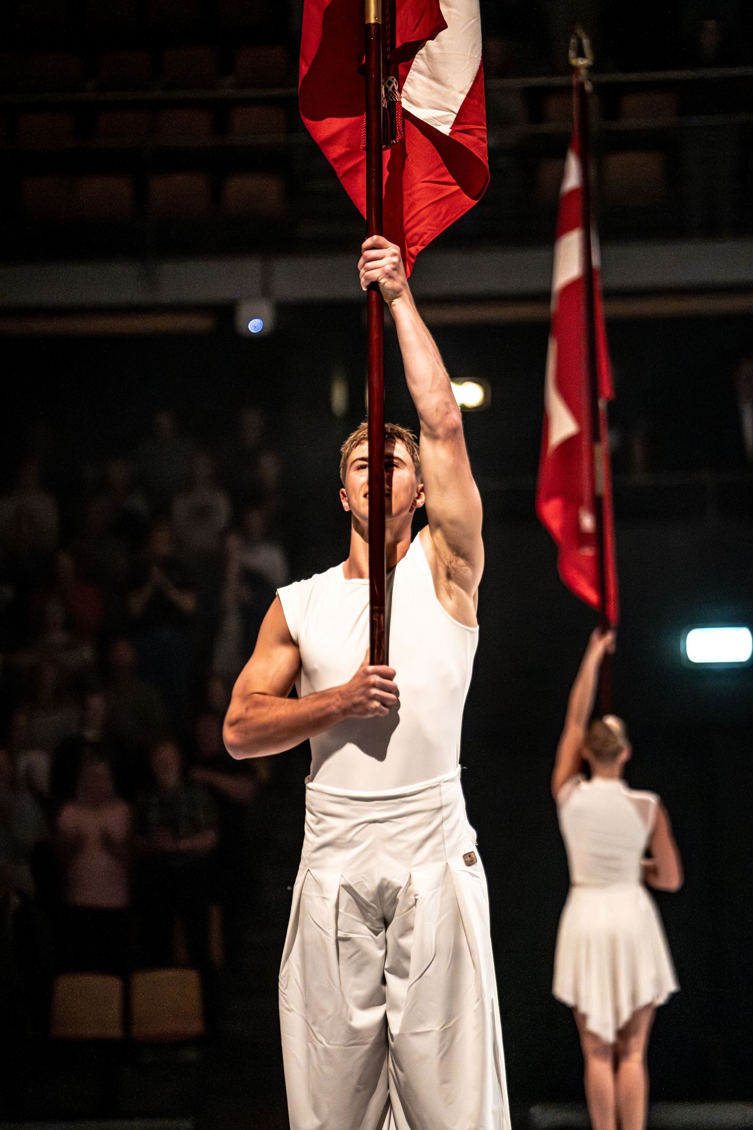 Male performer in white outfit holds red and white flag aloft on stage during a live performance.