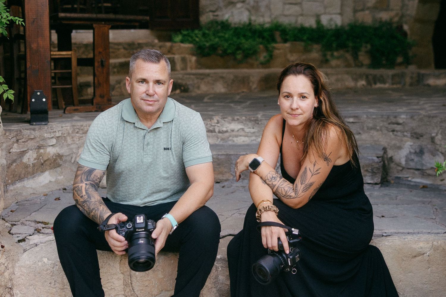 The Cyprus wedding photographers sitting together outdoors while holding camera equipment and drinks during a photo session.