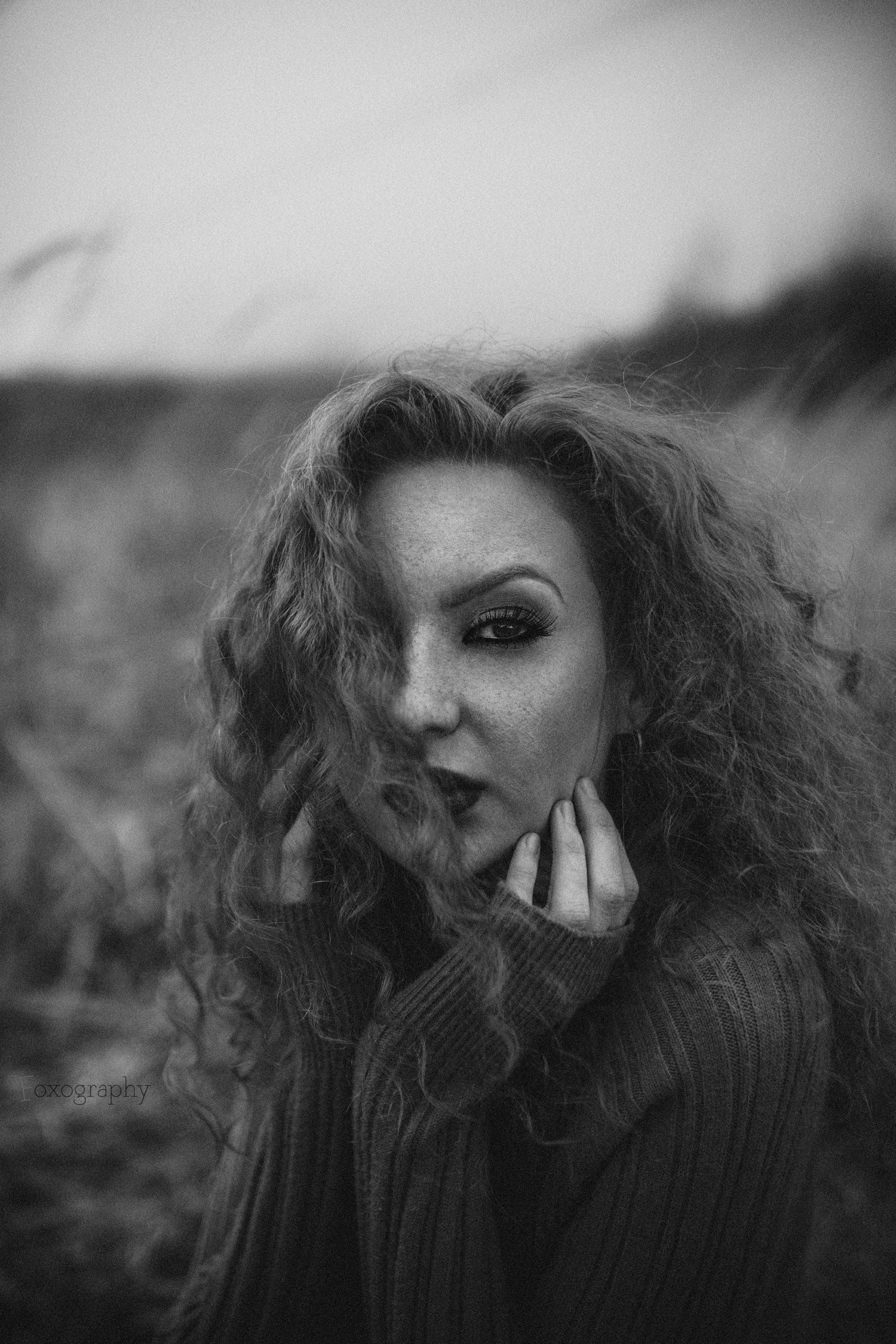 Čiernobiely portrét ženy s kučeravými vlasmi a dramatickým líčením v exteriéri. Svadobná fotografia a portréty, Žilina.