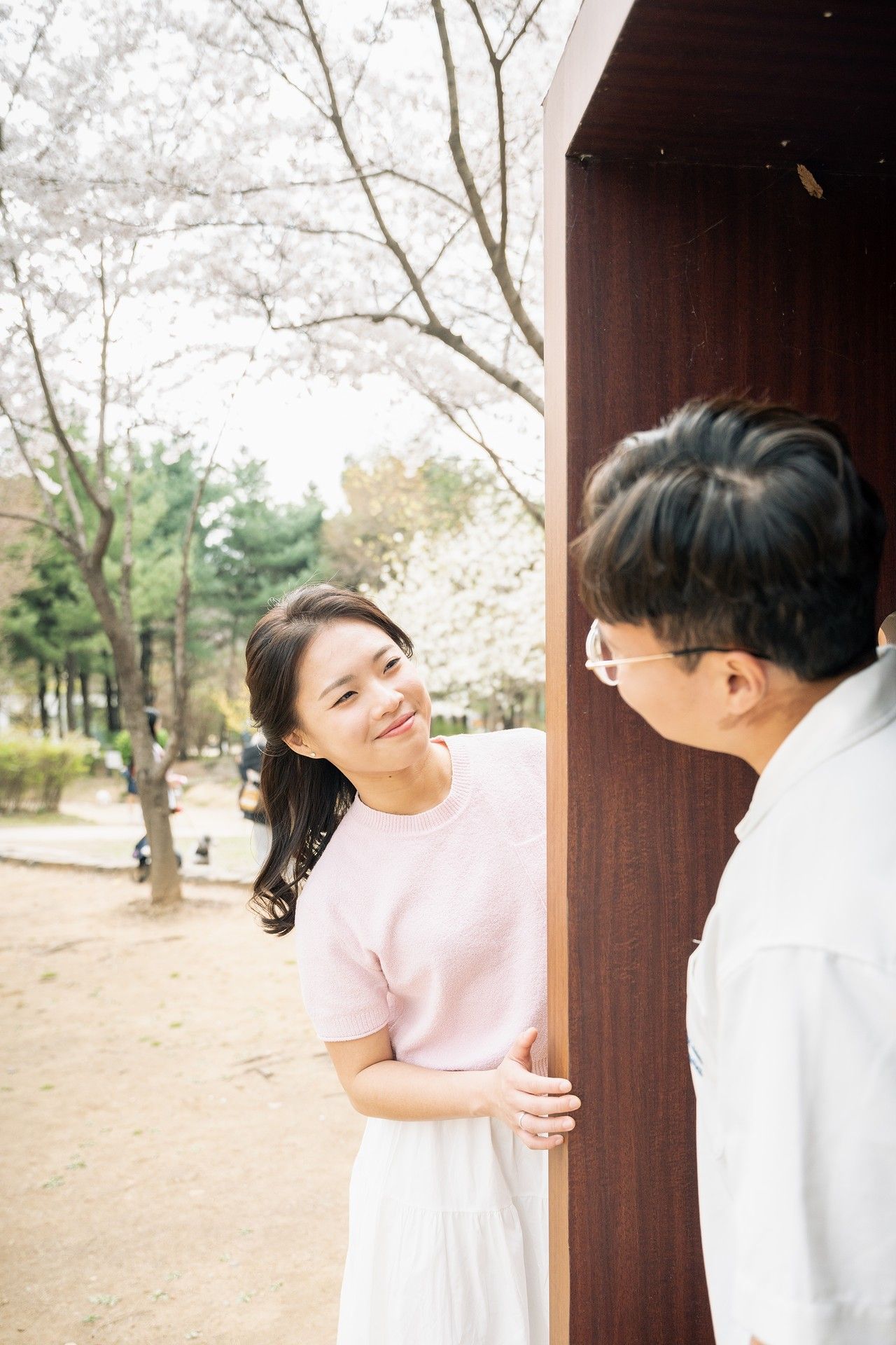 A playful sequence of photos showing a person peeking around a brown wooden door frame in a park setting.