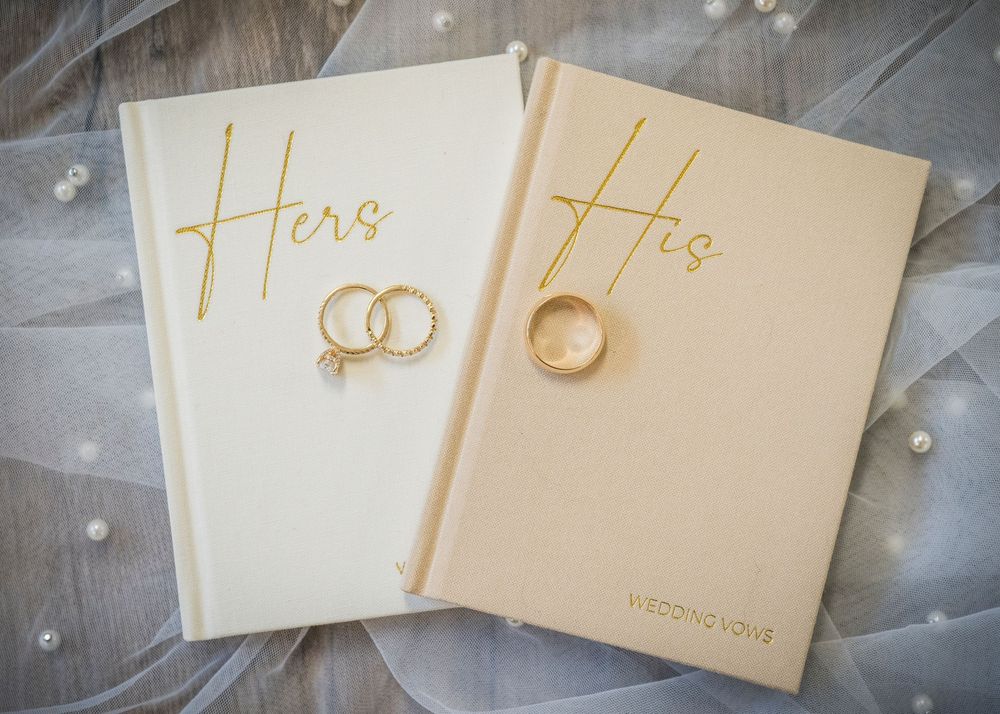 His and Hers gold wedding vow books with matching gold wedding bands on ivory fabric.
