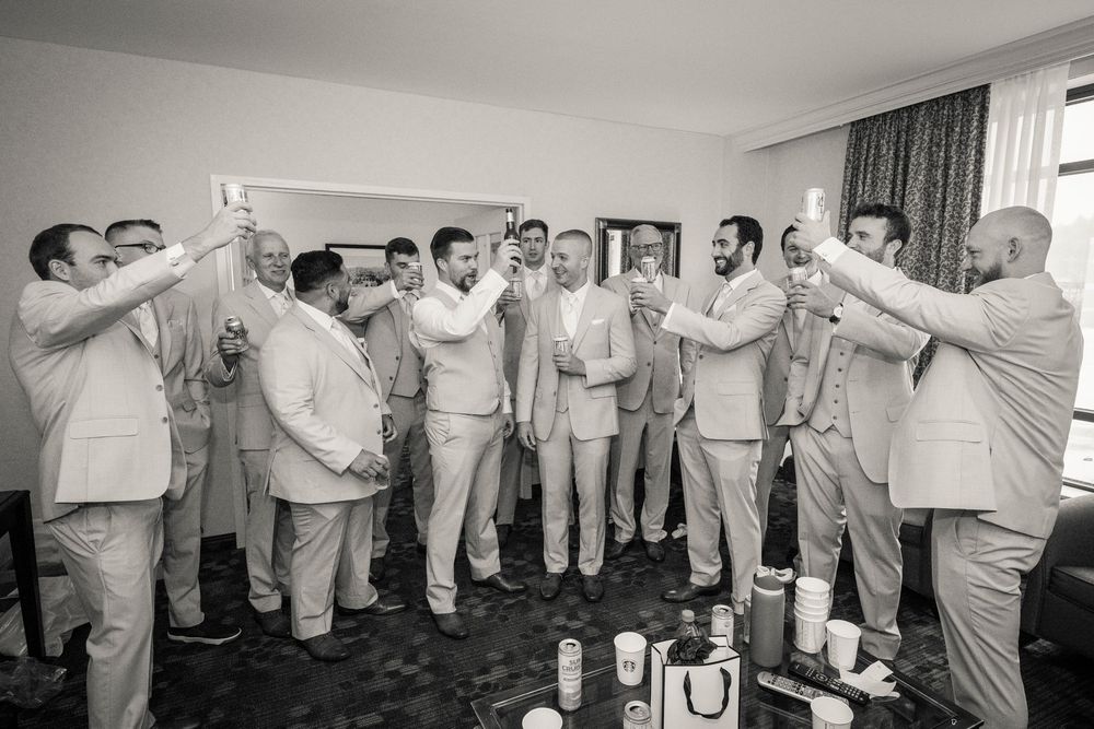 Groomsmen in suits raising glasses for a toast in a hotel room during wedding day preparations.