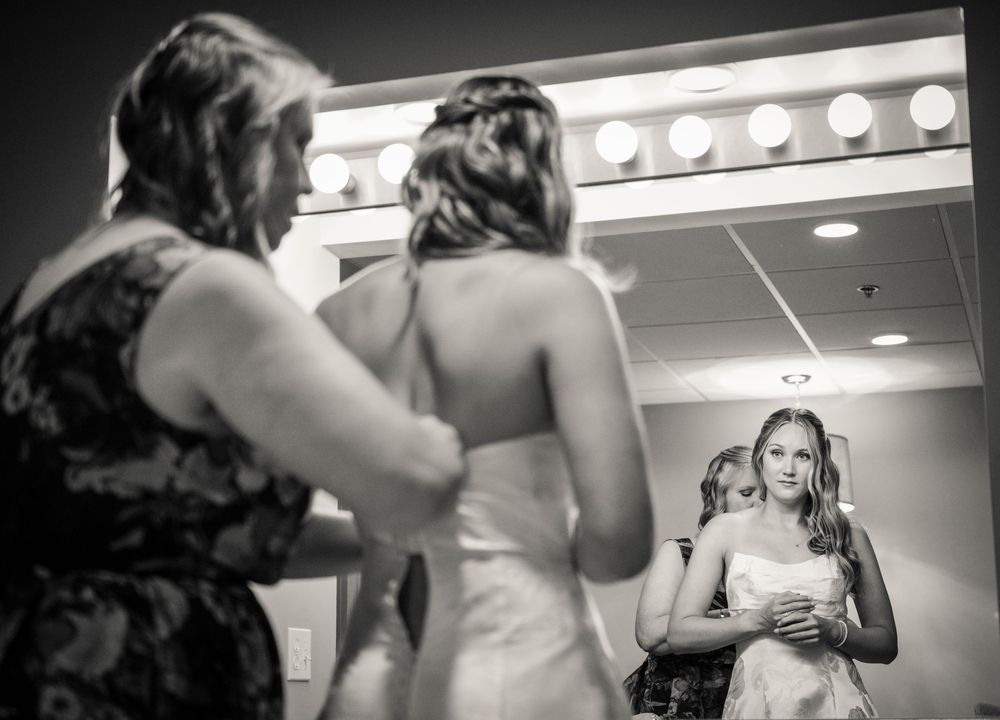 Black and white photo of bridesmaids helping bride get ready in a dressing room before the wedding ceremony.