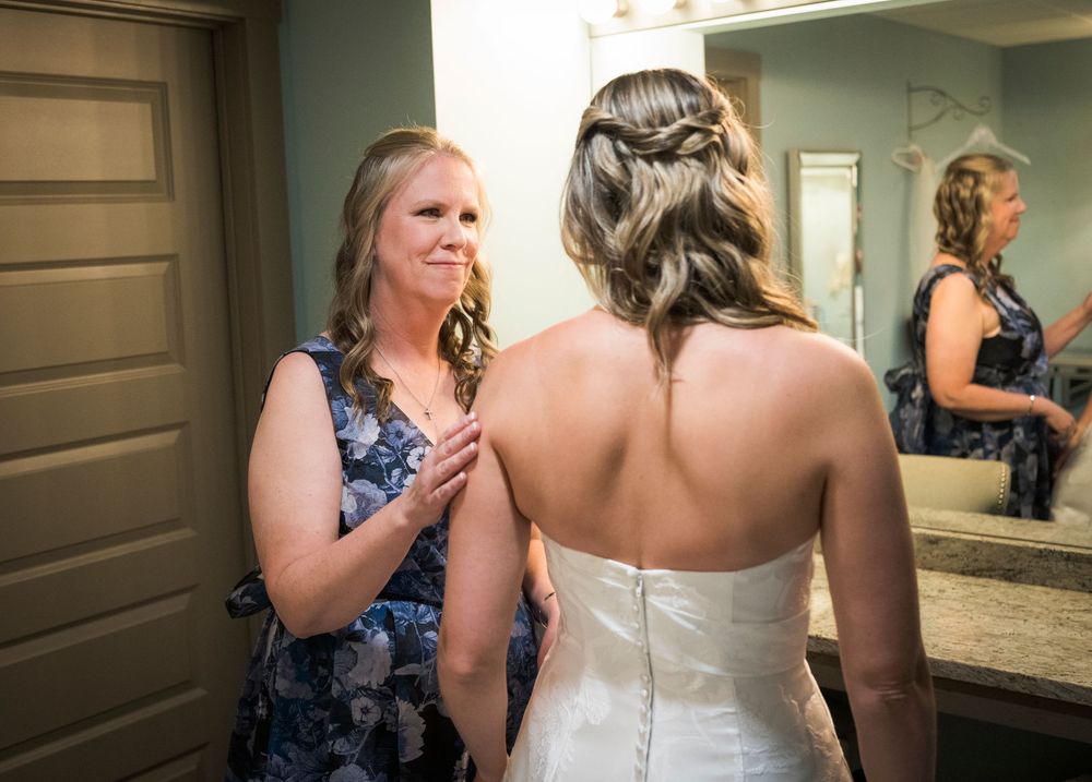 Woman in floral dress helping bride with strapless wedding gown during bridal preparations.