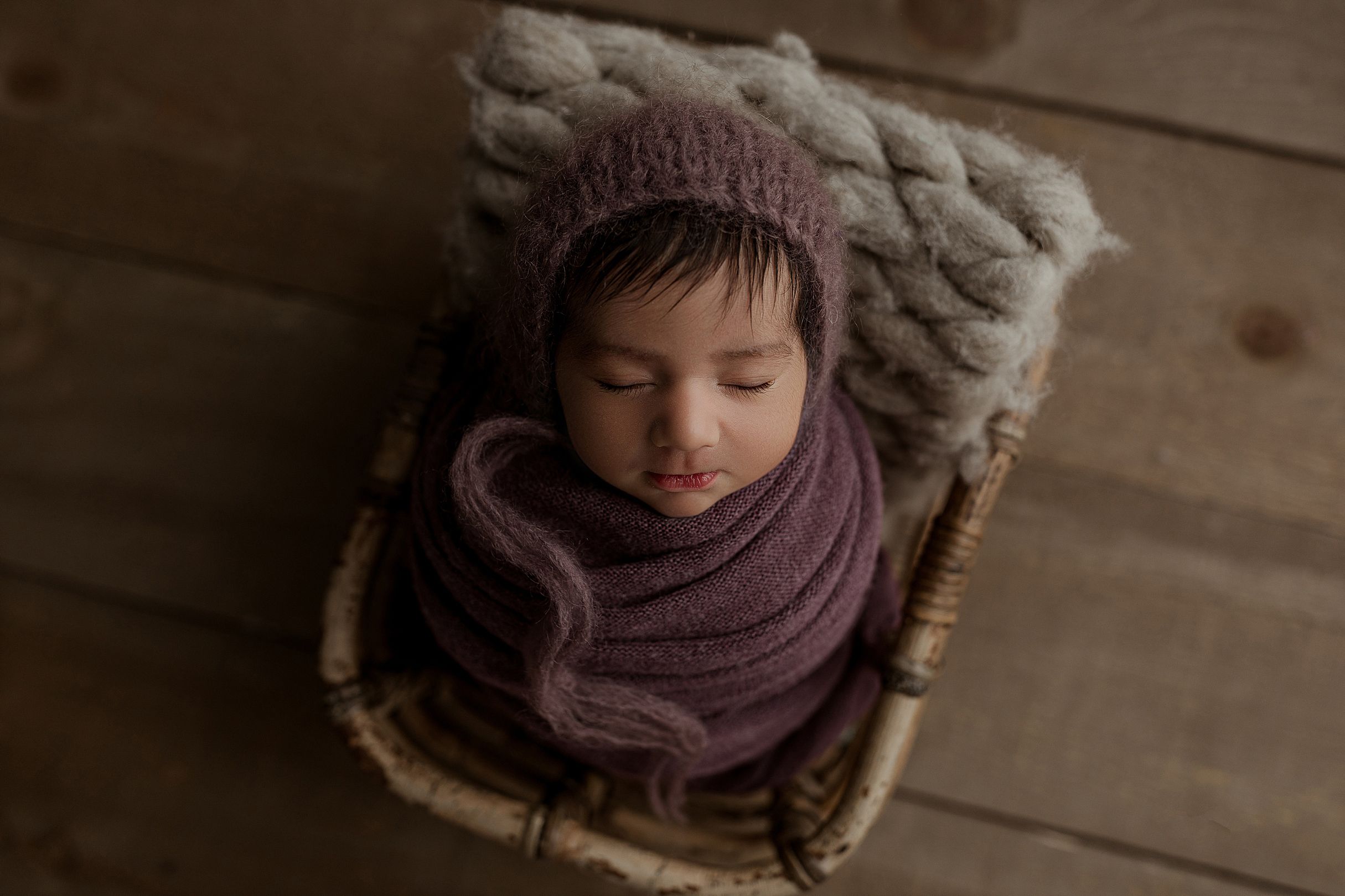 A person wearing a purple knit scarf and winter coat looks down thoughtfully against a wooden background.