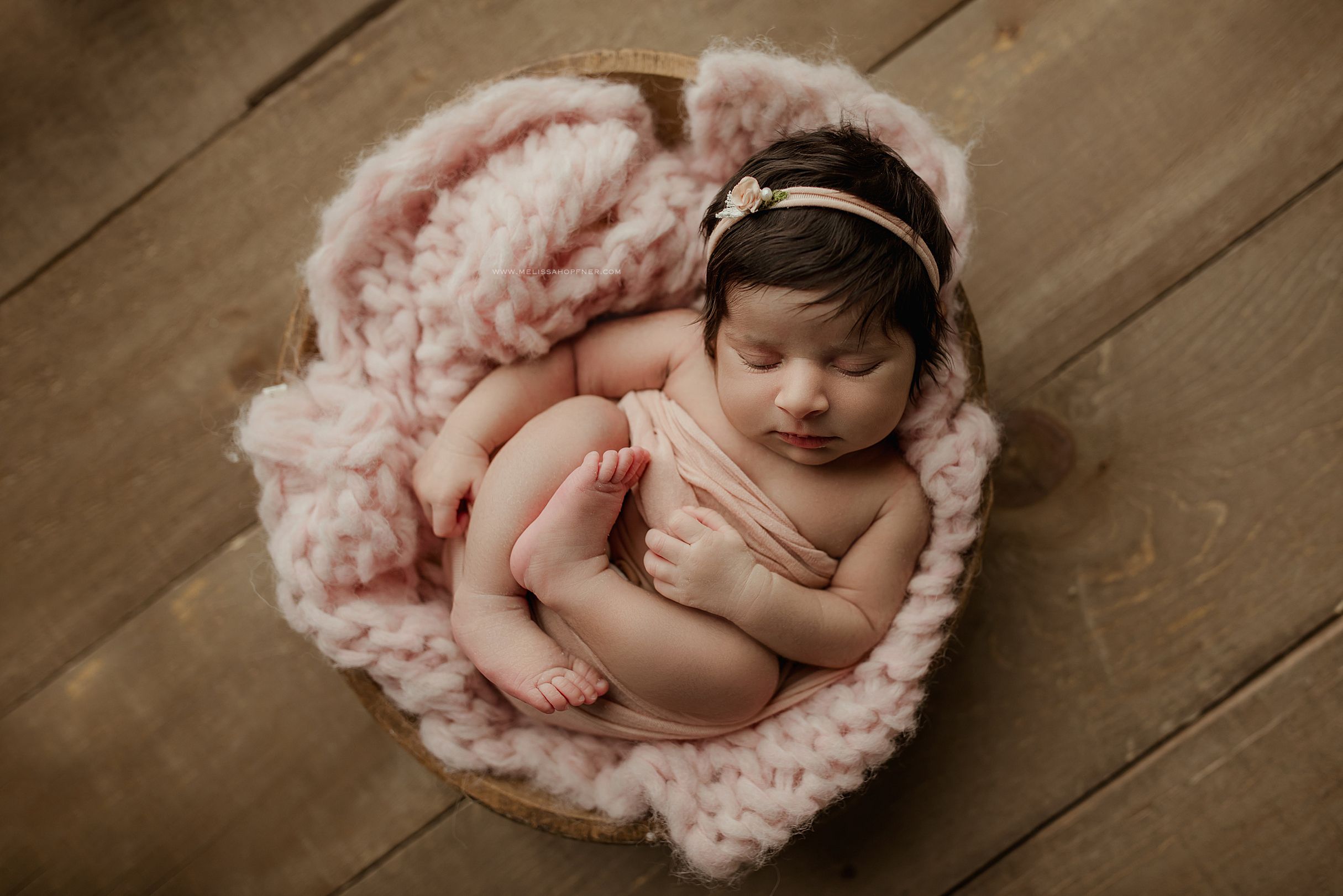 Newborn photography collage showing six poses of a sleeping baby in pink blankets on a wooden floor.