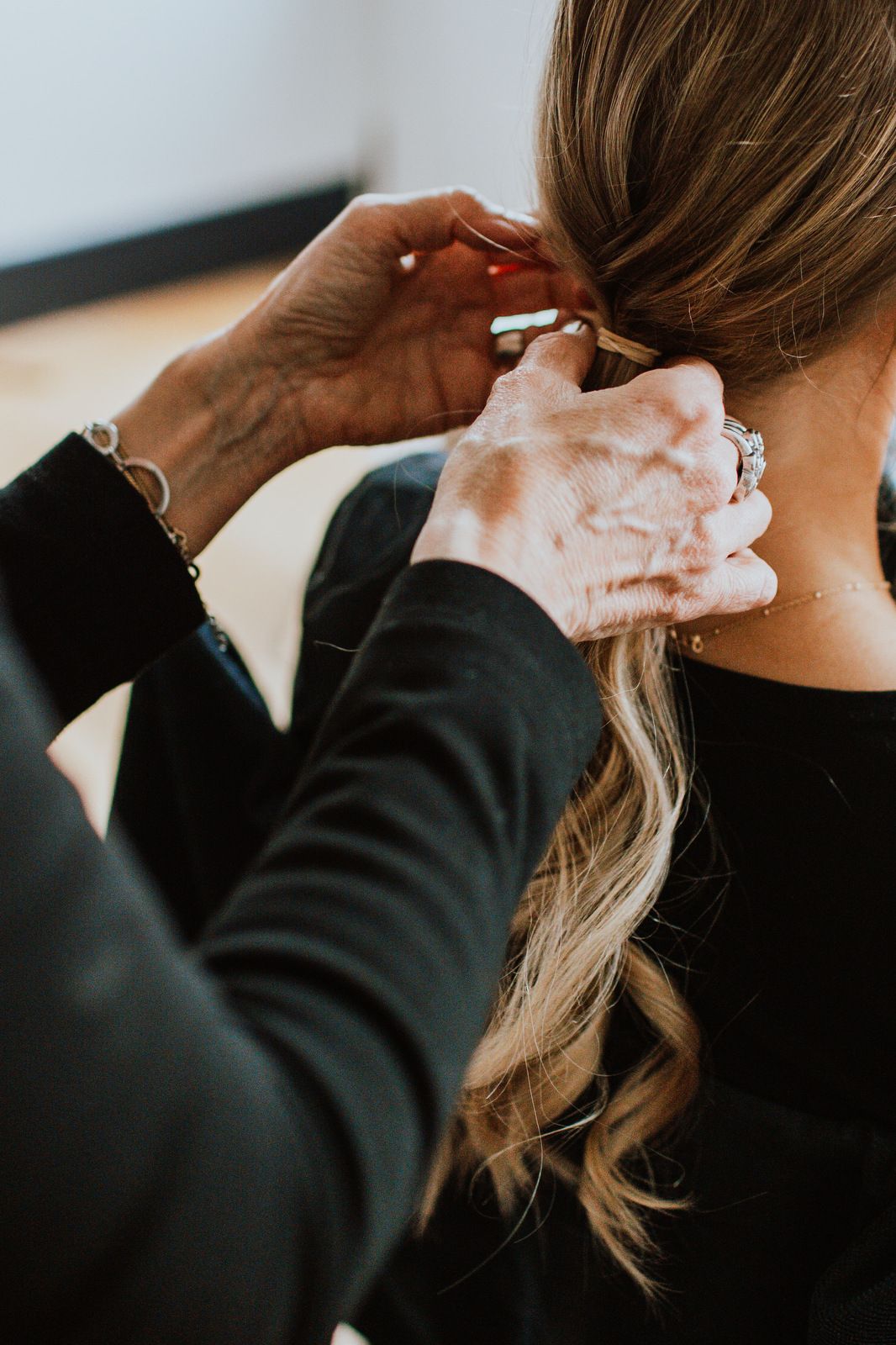 Close-up sequence showing hands styling long blonde hair against dark background in professional salon setting.
