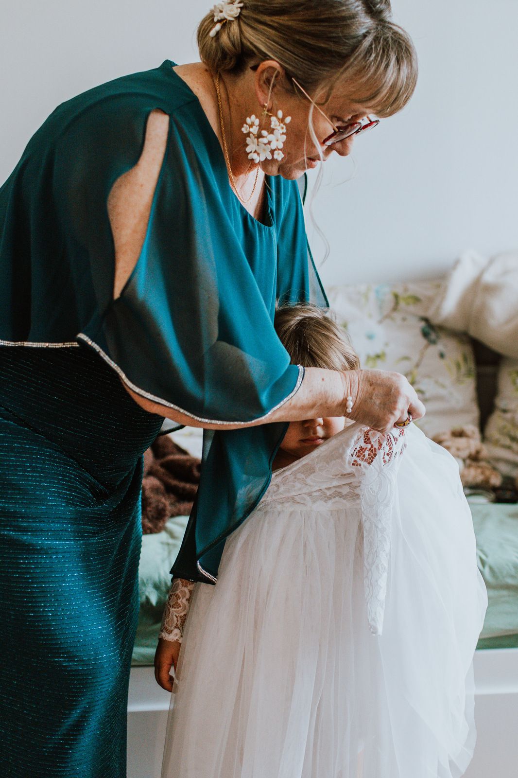 A person in a teal wrap helps adjust the details of a white lace wedding dress in a series of preparation photos.