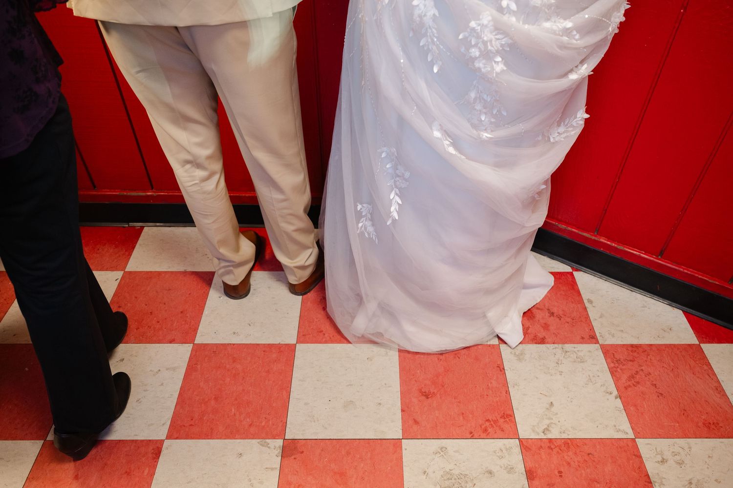 White wedding dresses and black suits create a striking pattern against a red and white checkered floor.