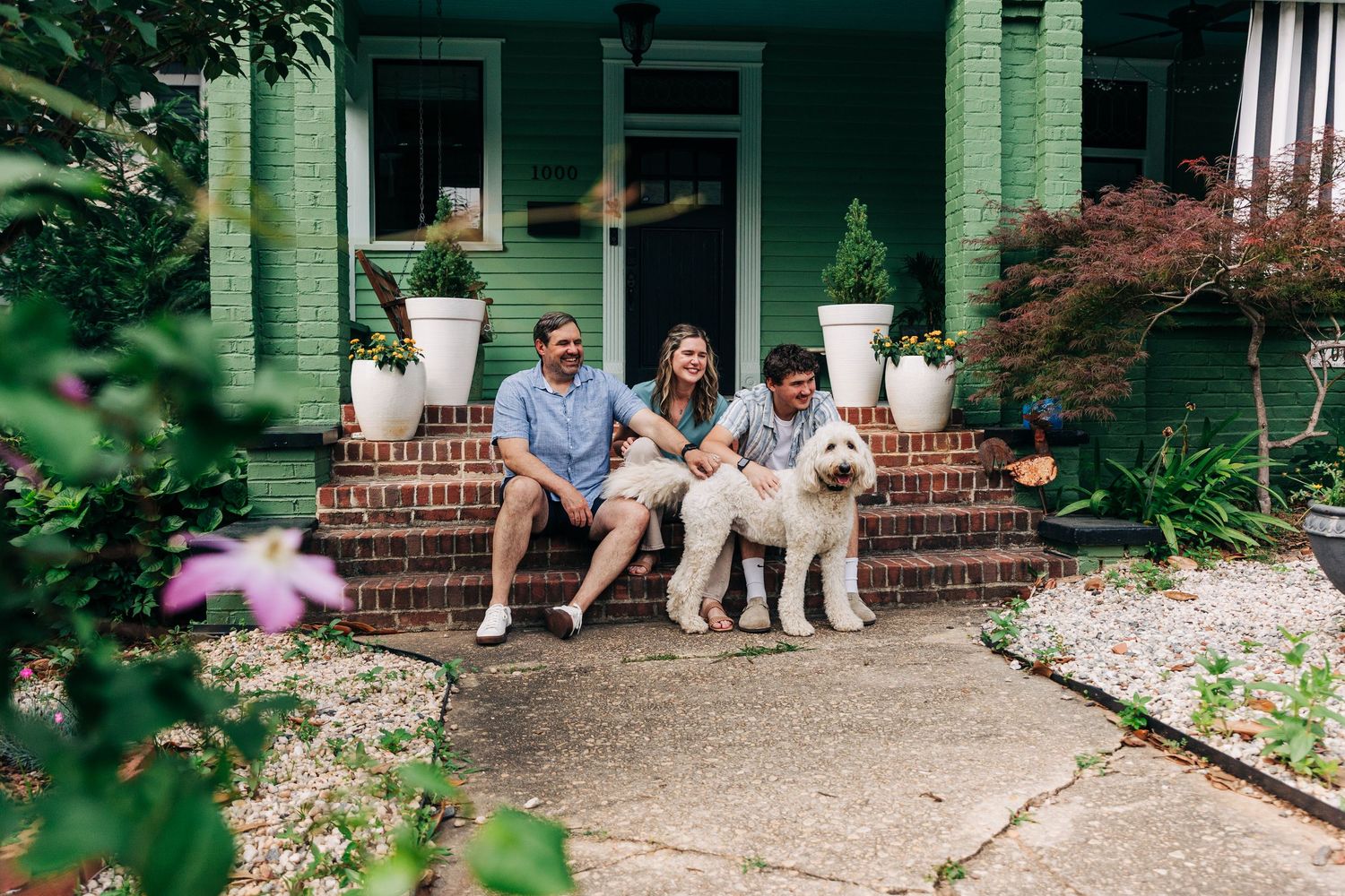 A Charlotte family relaxing on the steps of a house surrounded by lush greenery and landscaping.