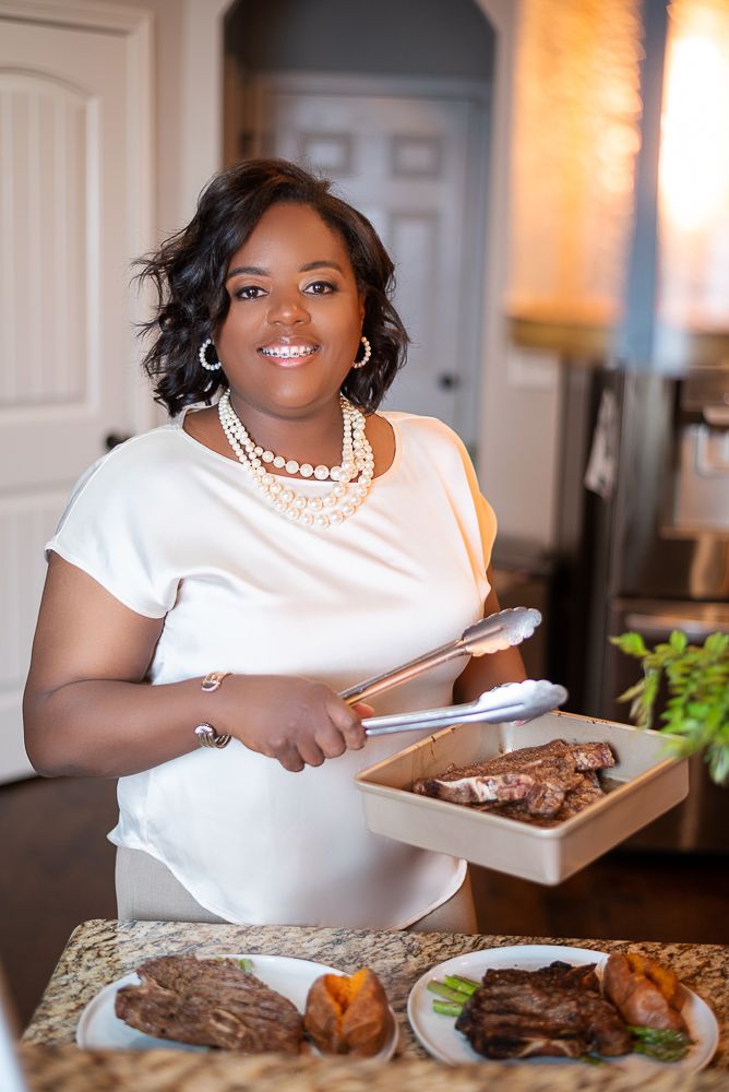 A person in a white dress enjoys a meal of steak and vegetables at a dining table.