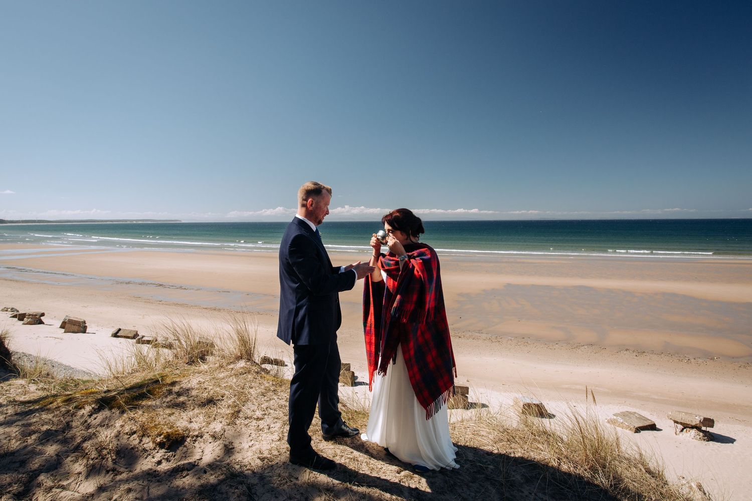 A couple shares an intimate moment on a sandy beach with ocean waves in the background.