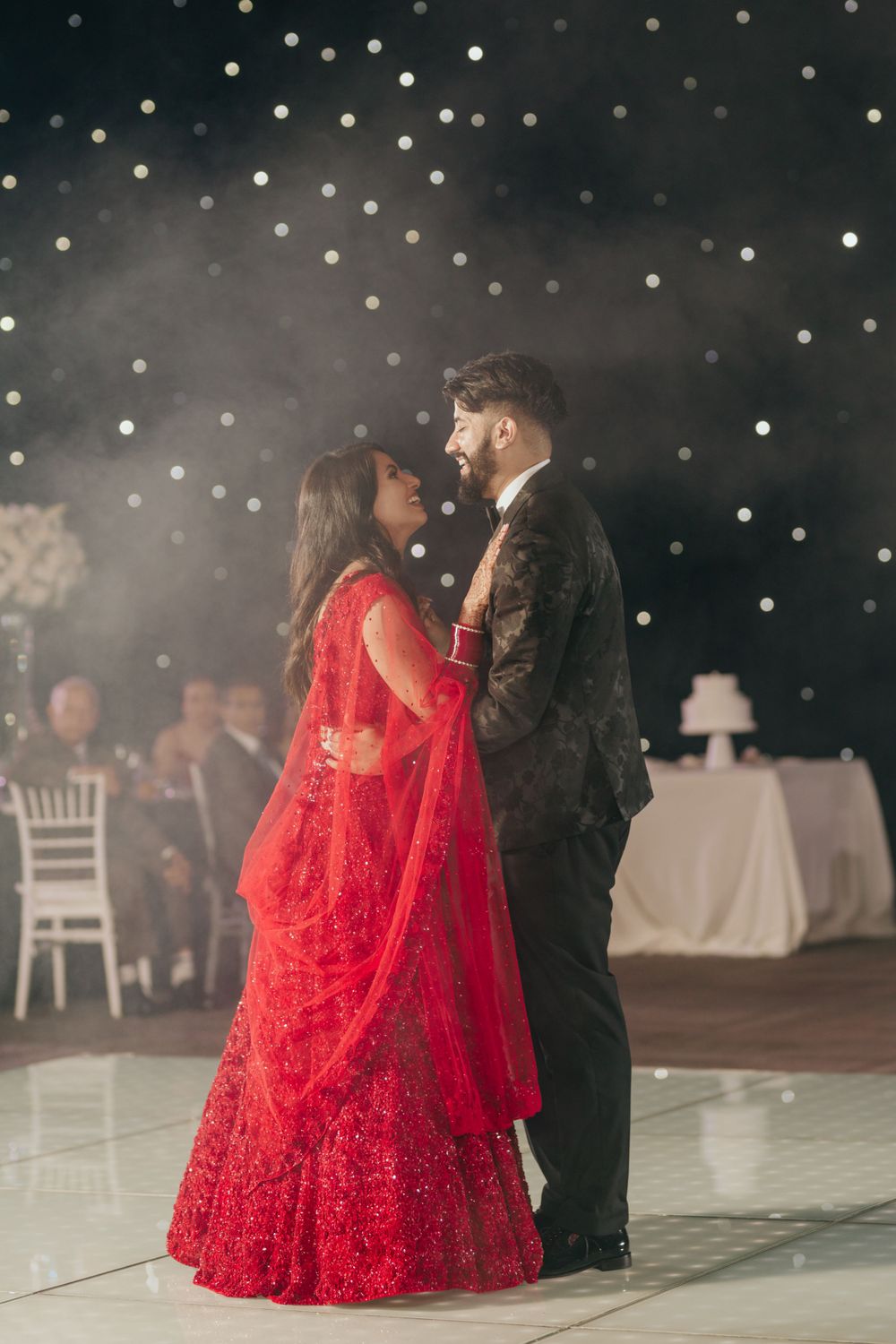 A couple shares an intimate dance moment at a wedding reception with twinkling lights above and a red bridal lehenga.