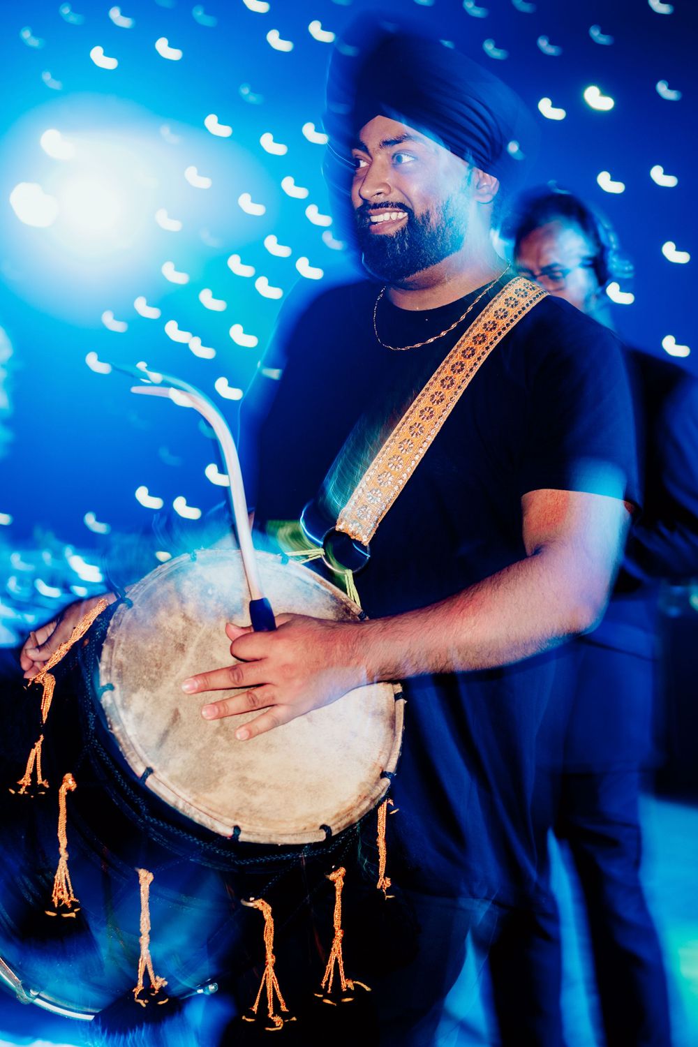 Musician performing with a djembe drum under blue stage lighting.
