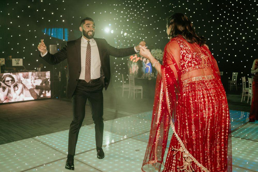 A couple dances together at a wedding reception with sparkly lighting and the bride wearing a stunning red lehenga.