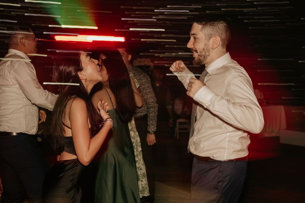 People dancing at a party with red and green lighting effects on a dark dance floor.