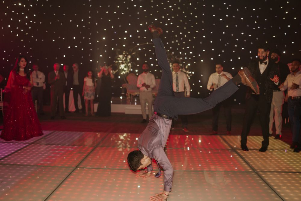 A person performs an impressive breakdancing move on an illuminated dance floor under twinkling lights at a formal event.