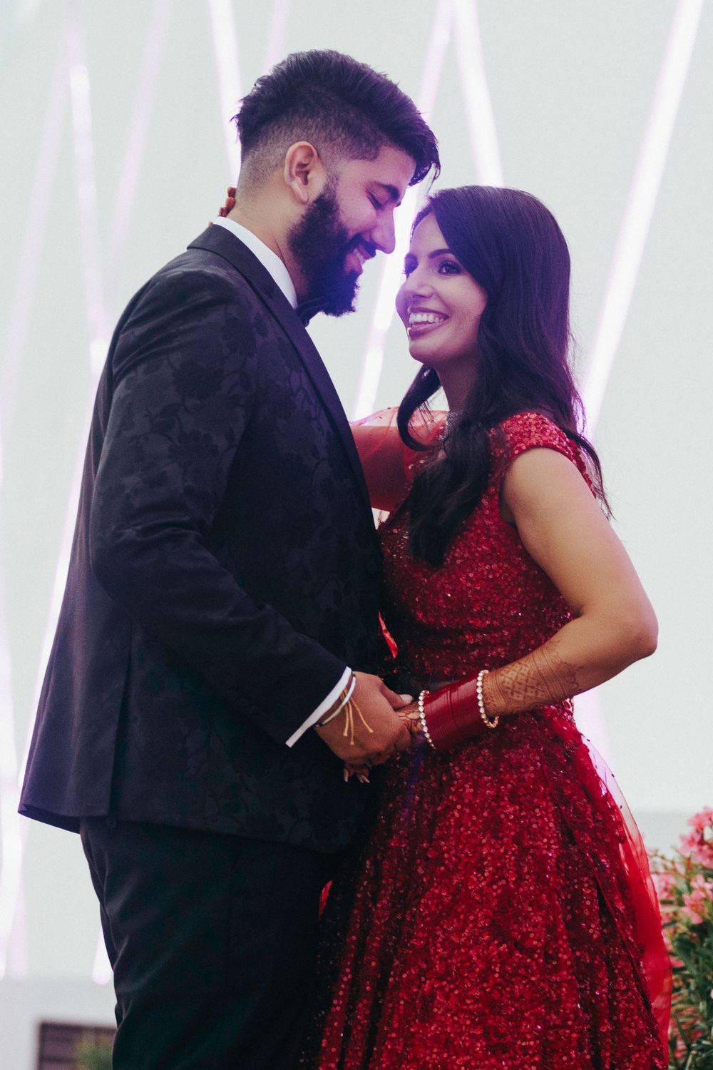A couple in formal attire share an intimate moment, with her in a sparkling red gown and him in a black suit.