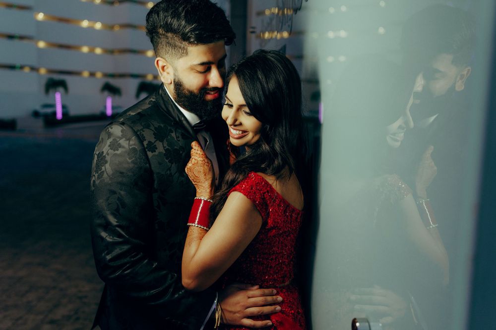 A romantic couple in formal attire share a tender embrace, with the woman wearing a vibrant red dress against a dark background.