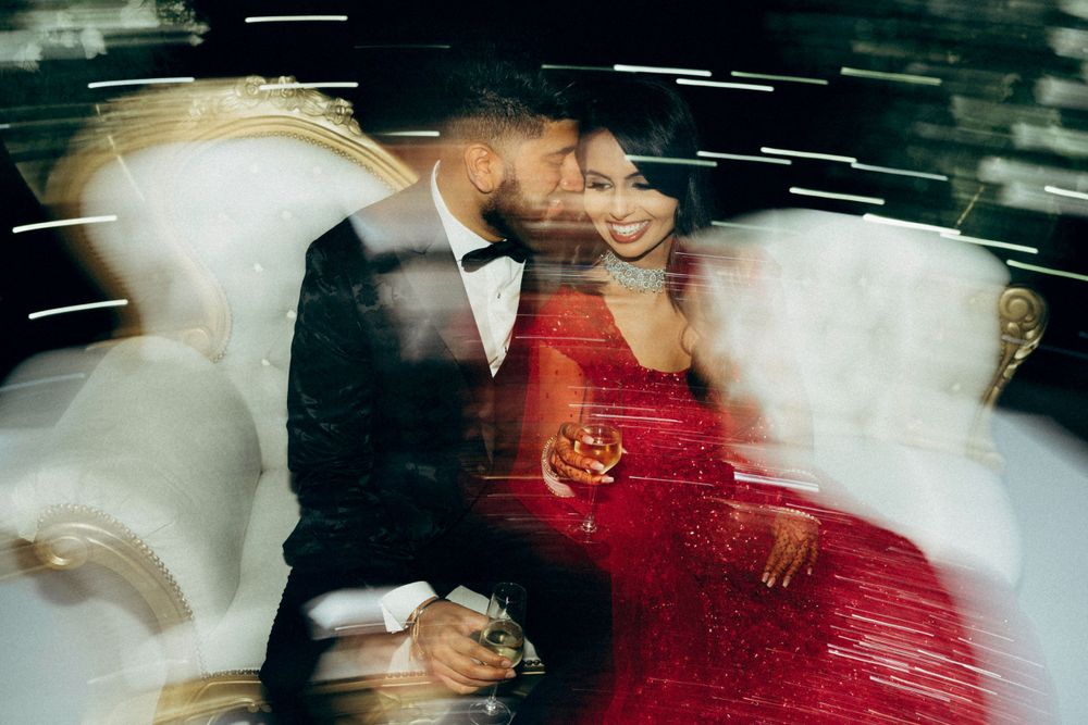 Motion blur captures a romantic moment between couple in formal attire with person in red dress seated on ornate chair.