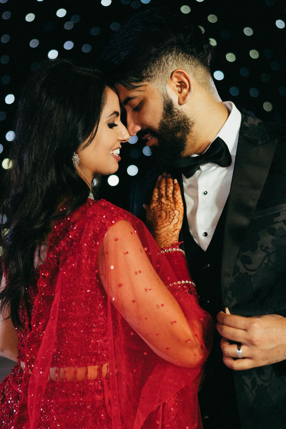 Romantic wedding couple in traditional South Asian attire sharing an intimate moment with sparkling lights in background.