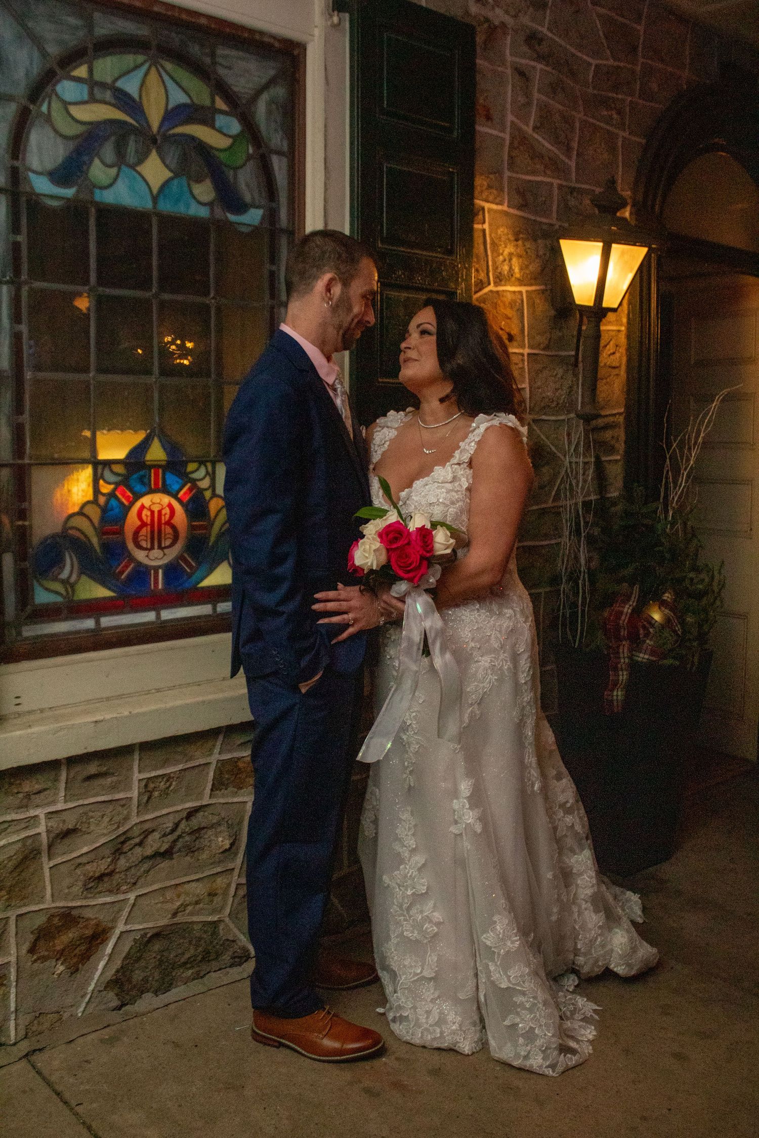 Couple posing by a stained glass window at night with atmospheric lighting.