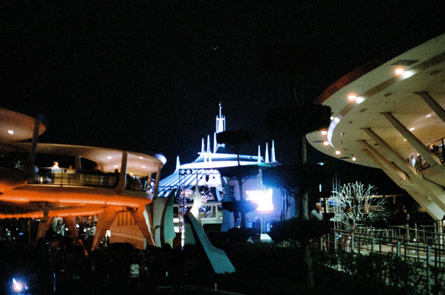 Illuminated Space Mountain and Tomorrowland buildings at Disney theme park glowing bright blue at night.