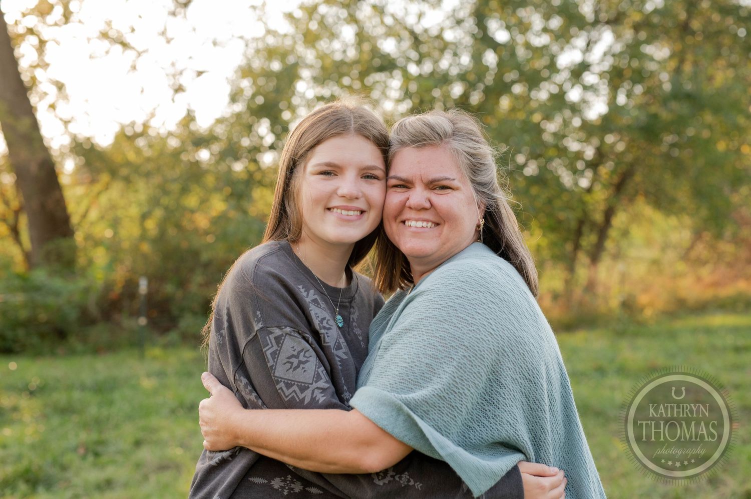 Two people share a warm embrace while smiling in front of autumn foliage.