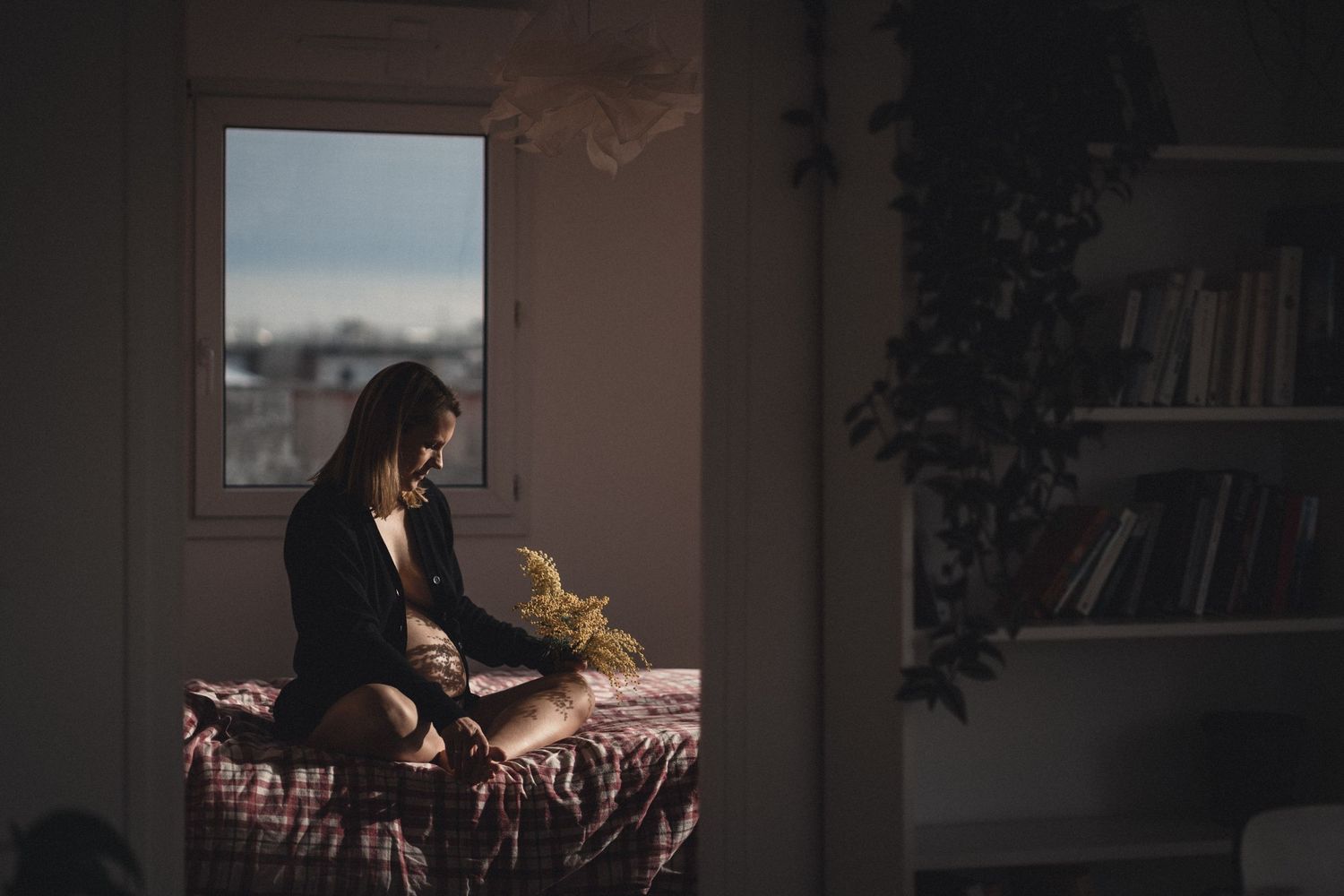 Femme enceinte assise sur son lit tenant un bouquet de mimosa fleurs, baigné d'une lumière naturelle