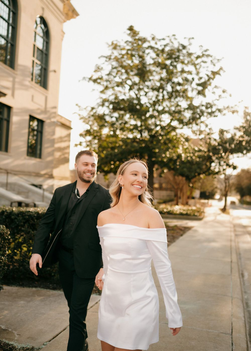 A couple shares a joyful moment while walking along a building with classical architecture in Charlotte, North Carolina