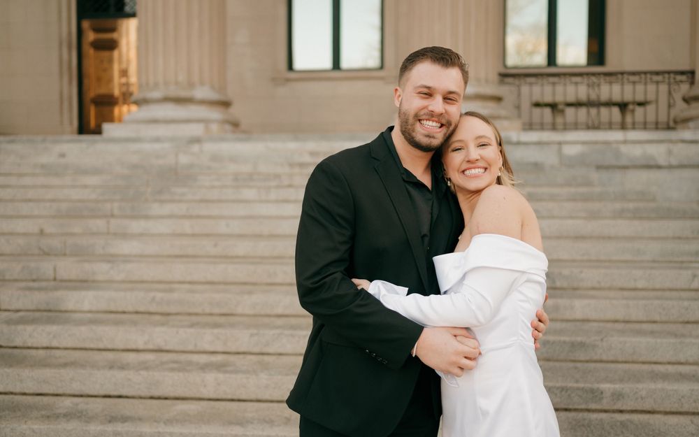 Couple in formal wear embracing on classic stone building steps.