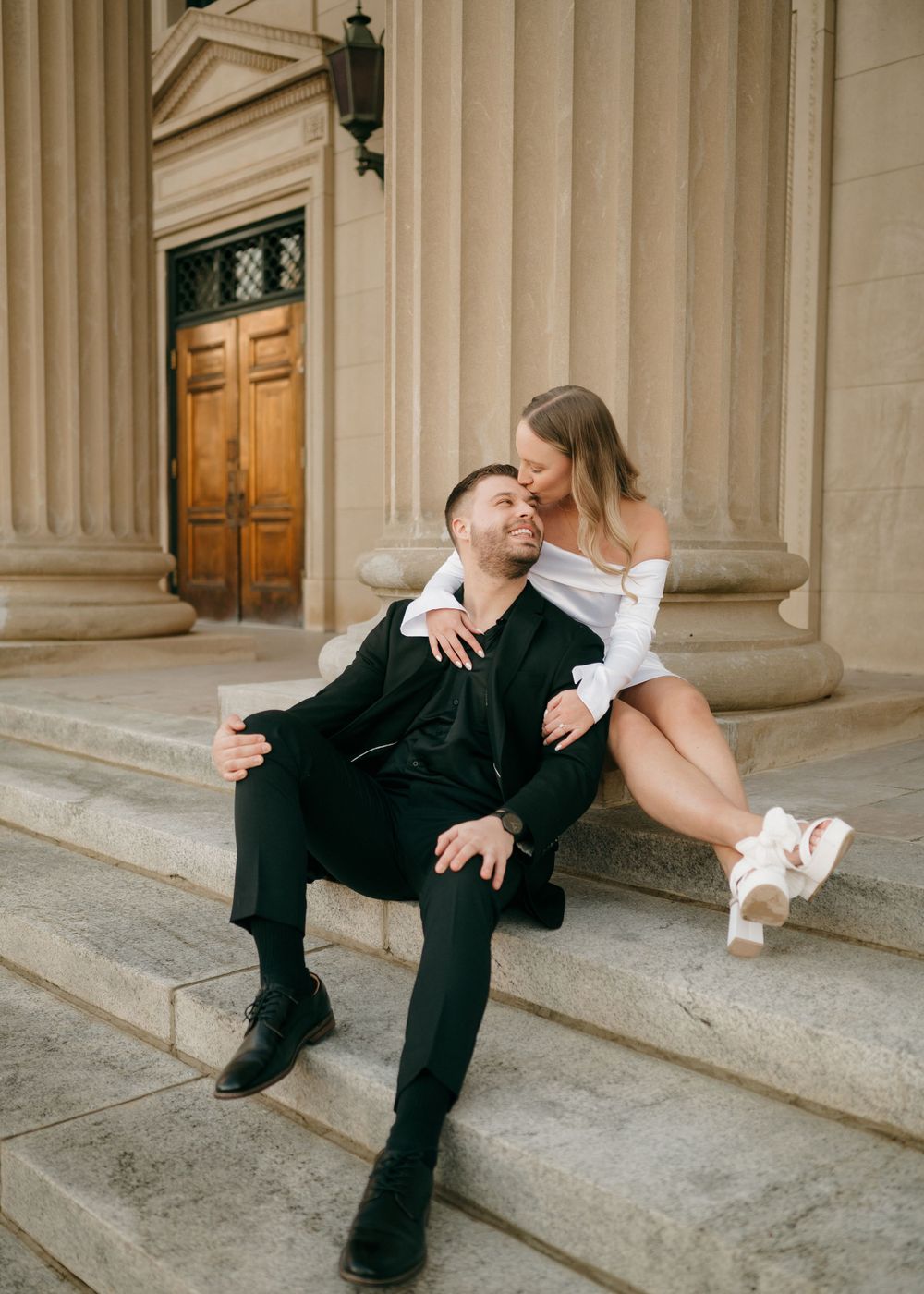 A tender moment captured on grand architectural steps with classical columns and wooden doors.