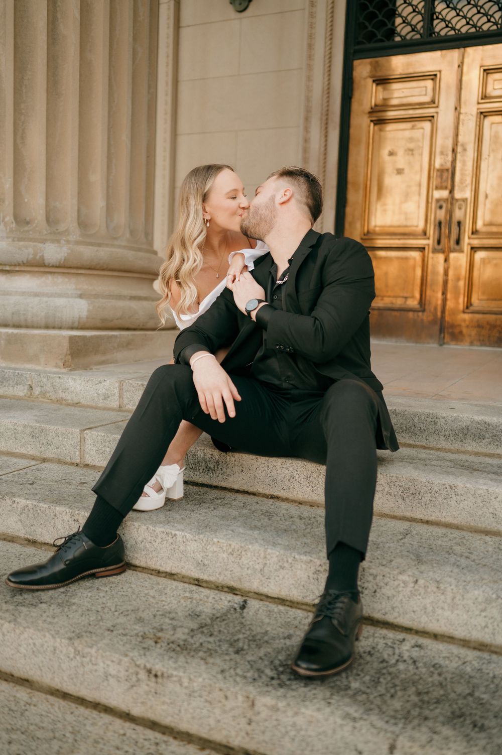 A romantic couple shares an intimate moment while sitting on stone steps in front of vintage doors in Charlotte
