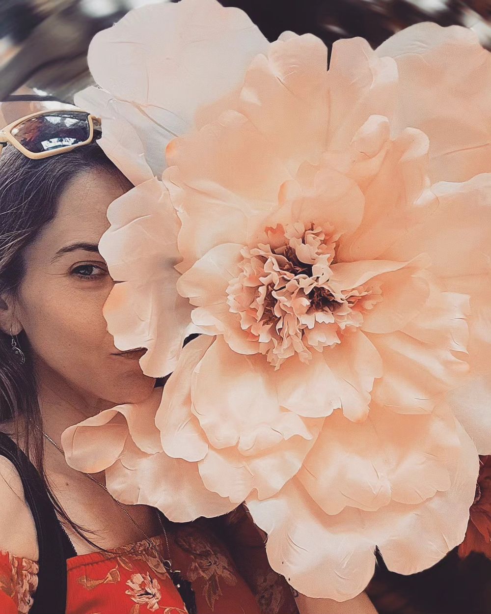 A large peachy-pink paper flower with delicate ruffled petals shown in close-up detail against a blurred background.