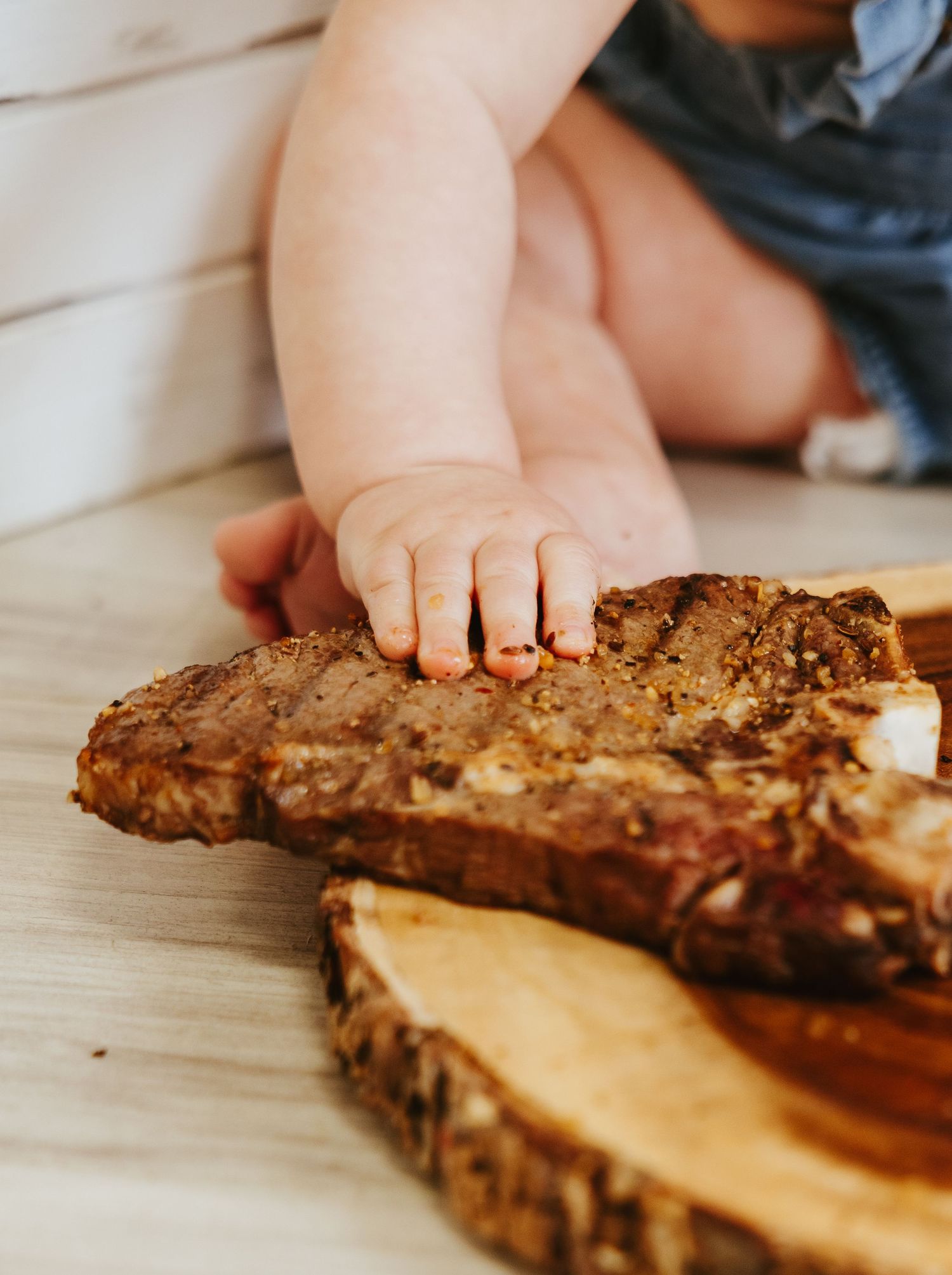 Small hand reaching for grilled sandwich on wooden serving board.