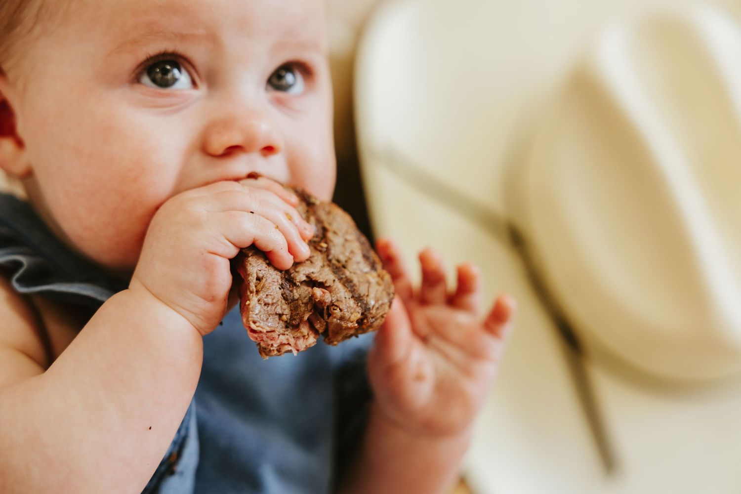 Baby eating grilled sandwich while wearing blue romper.