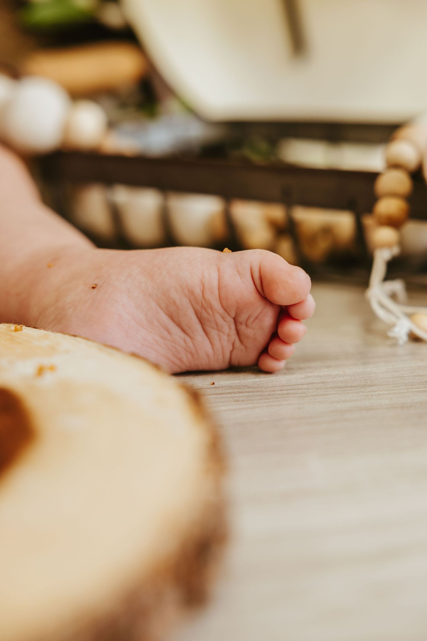 Close-up of baby foot next to wooden serving board on floor.