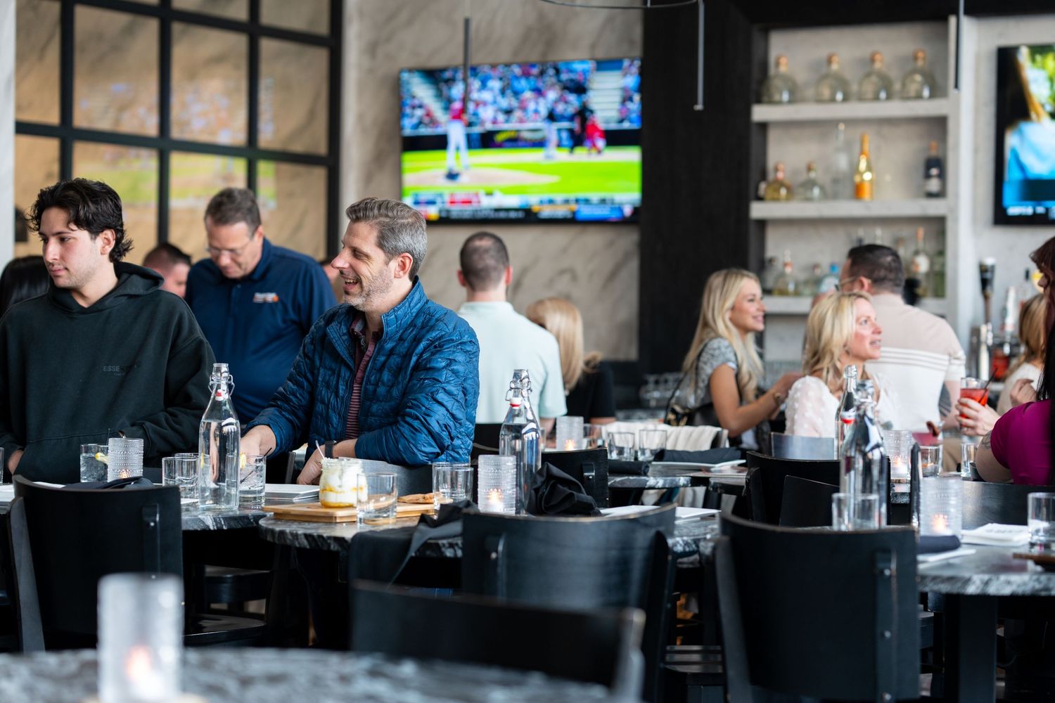Diners seated at a modern sports bar with multiple TV screens and contemporary decor in the background.