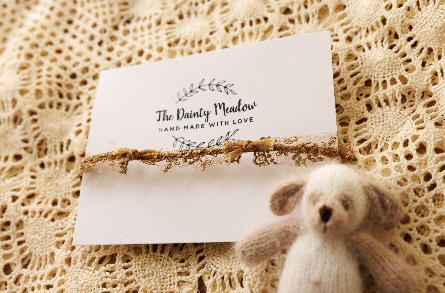 A small white teddy bear rests next to a business card on delicate lace fabric.