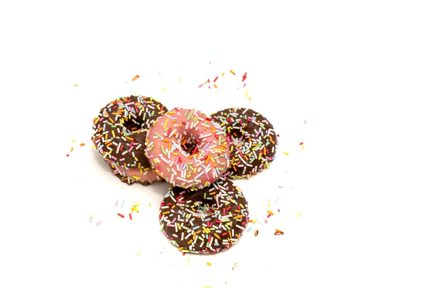 "Vier donuts, drie met chocoladeglazuur en eentje met roze, allemaal bedekt met kleurrijke hagelslag. Een vrolijke en lekkere snack!"