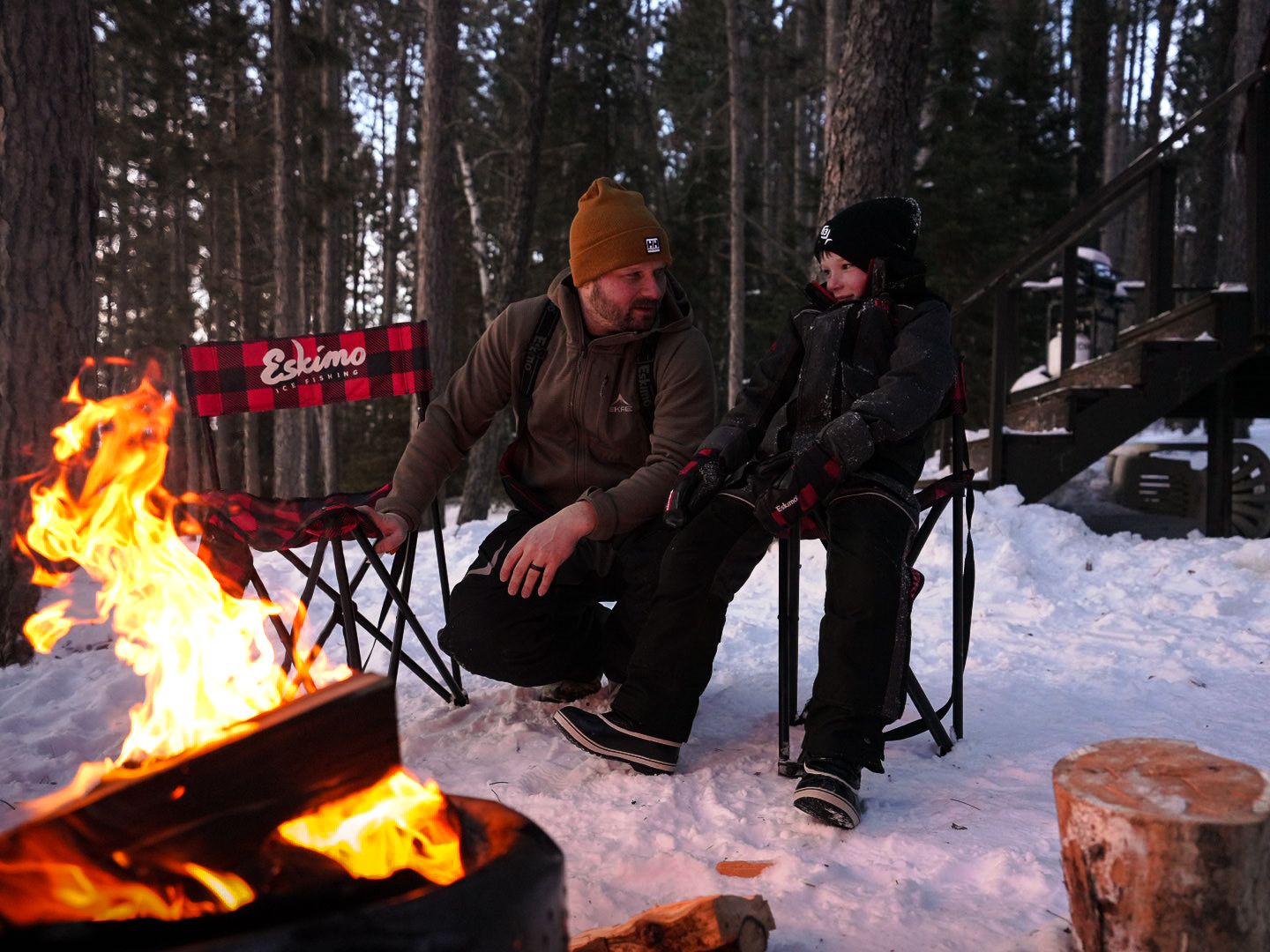 Campfire burning brightly in snowy forest setting during winter evening.