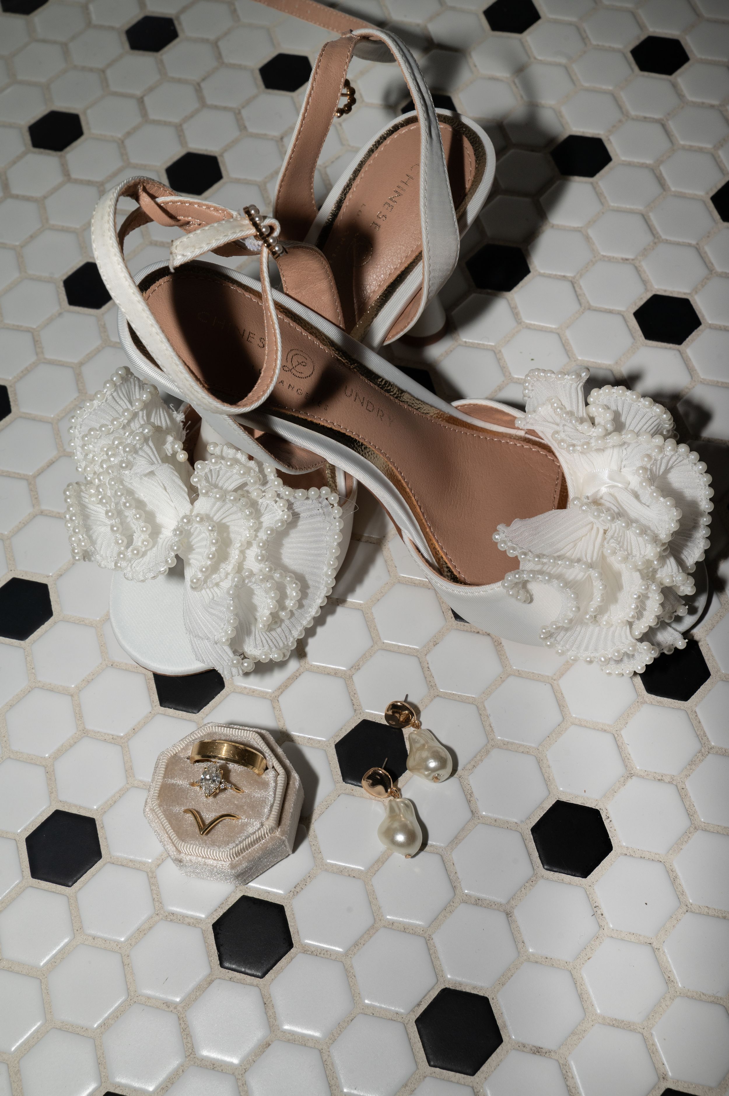 Elegant bridal shoes and accessories arranged on a hexagonal tile floor.