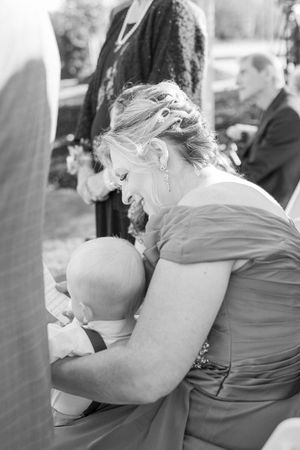 A tender moment between a woman in a formal dress and a baby at what appears to be a wedding celebration.